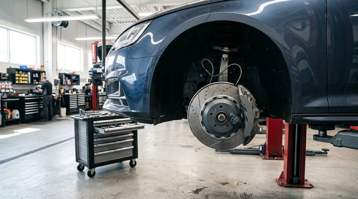 Mechanic inspecting an Audi Big Brake Kit caliper and two-piece rotor mounted behind an alloy wheel