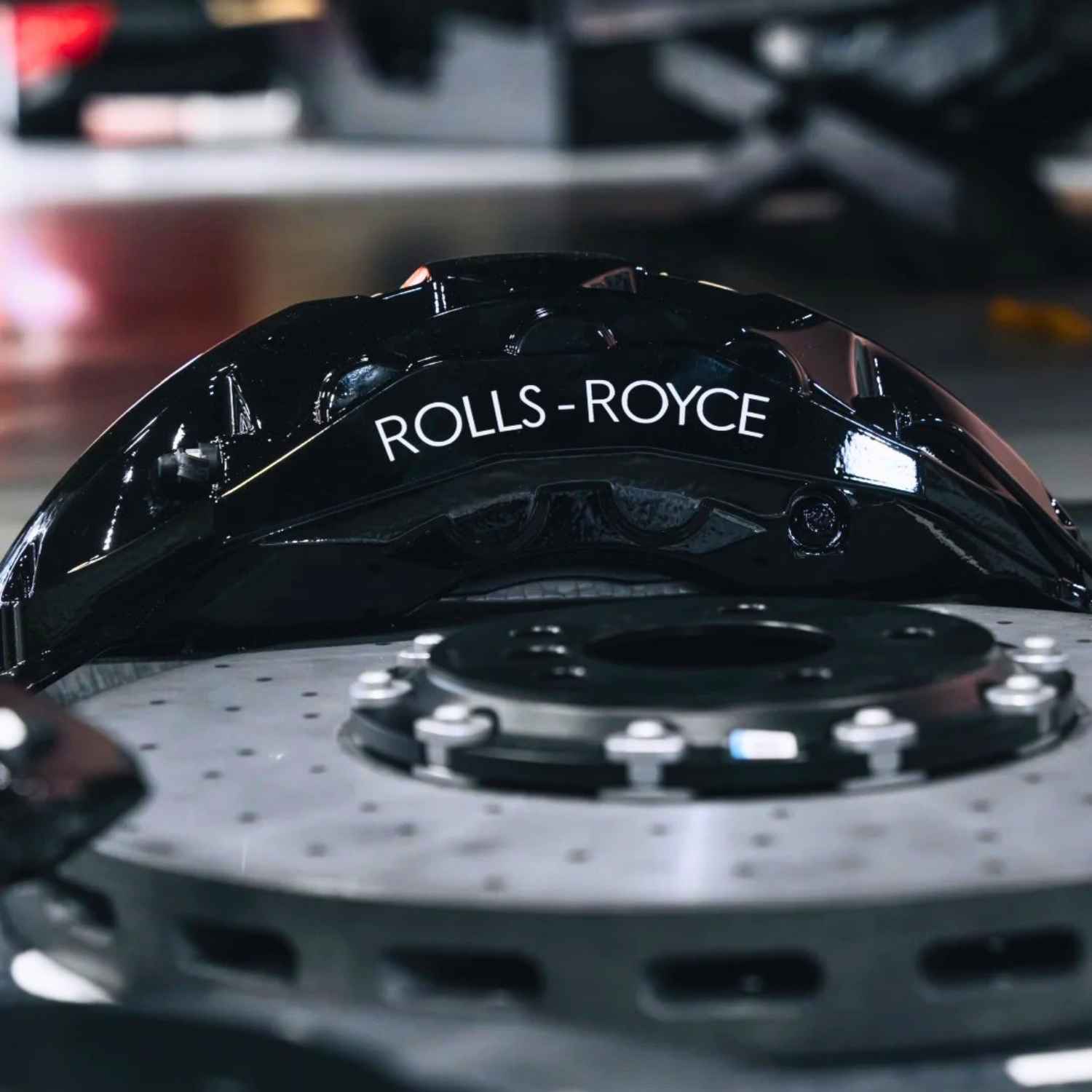 Close-up of a ForzaCCB carbon ceramic brake rotor paired with a gloss black Rolls-Royce brake caliper.