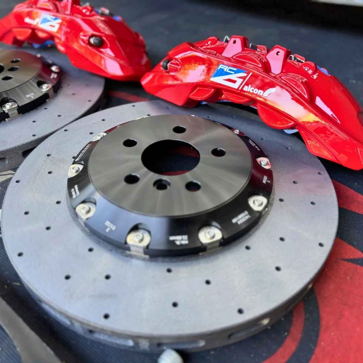 Pair of ForzaCCB carbon ceramic brake rotors showcased with bright red Alcon RCZ forged 6-pot brake calipers.